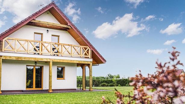A two-story house with a wooden balcony, large windows, and a well-maintained lawn.