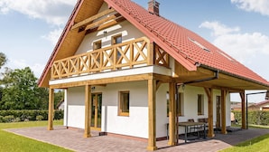 A two-story house with a red-tiled roof, wooden beams, and a covered patio area with a table and chairs.