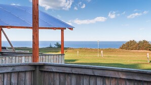 Eine Holzterrasse mit einer Solarzellen-Dachkonstruktion, mit Blick auf eine Rasenfläche und den Ozean.