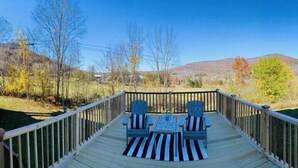 Eine Terrasse mit zwei Stühlen und einem Tisch, mit Blick auf eine reizvolle Landschaft aus Bäumen und Hügeln.
