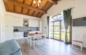 A modern kitchen with white cabinets, a wooden ceiling, and a dining area with a wooden table and chairs.