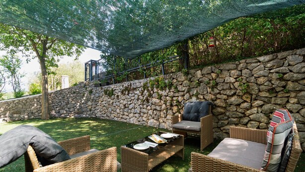 An outdoor patio with wicker furniture, a stone wall, and a green net overhead. - Stunning apartment in Kucice (Kucice)