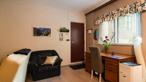 A furnished room with a leather sofa, a wooden desk, a chair, a bed, a door, and a window with blinds. - Stunning apartment in Kucice (Kucice)