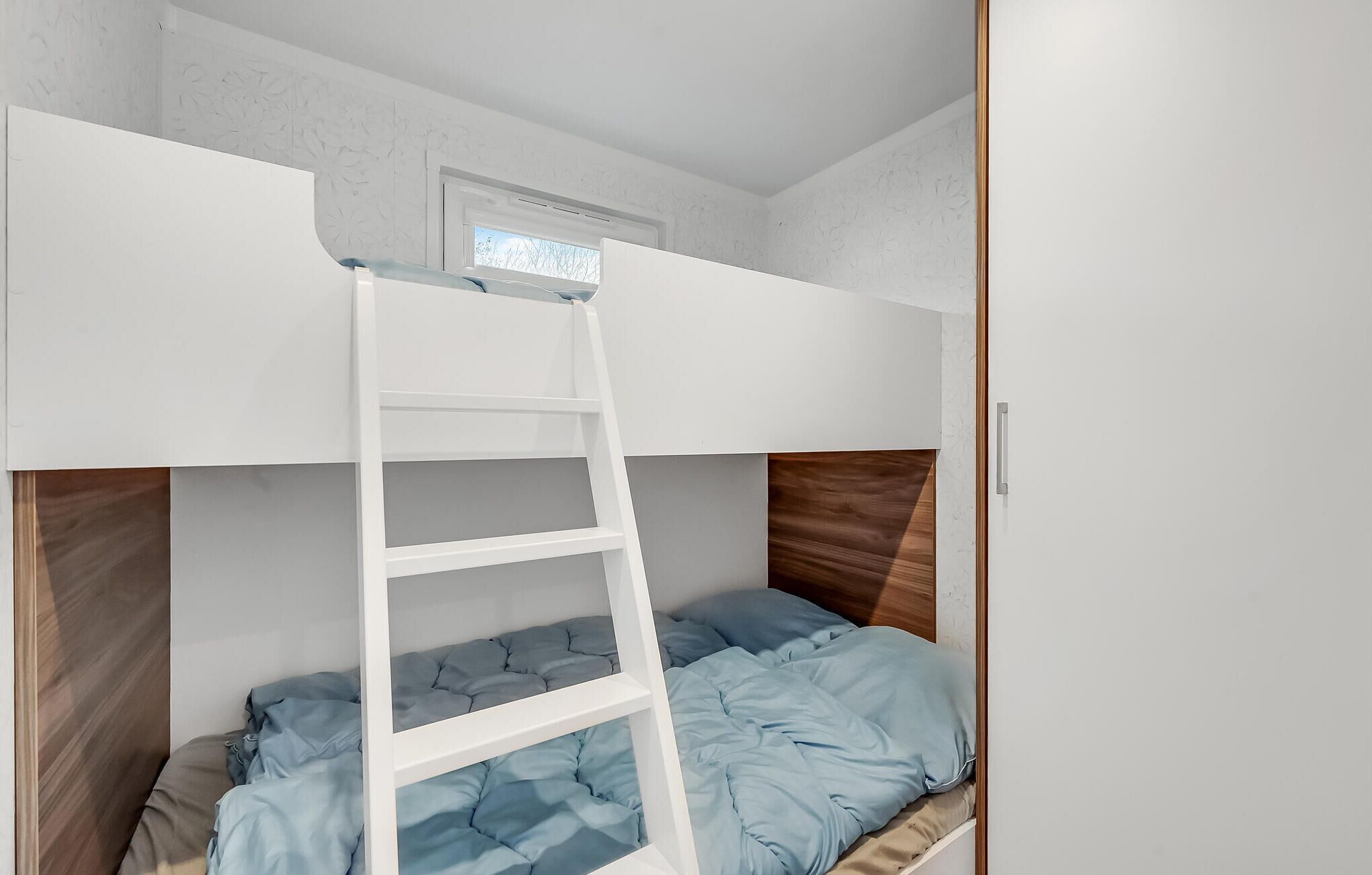 Un lit superposé avec une échelle, une tête de lit en bois et une fenêtre au-dessus du lit supérieur.
