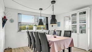 Ruokailutilassa on kuudelle katettu pöytä, mustat tuolit, vaaleanpunainen pöytäliina ja viinipullo. Pöydän yläpuolella on kaksi riippuvalaisinta, ja oikealla puolella on valkoinen kaappi, jossa on lasiovet.
