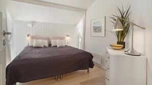 Een slaapkamer met een bed, nachtlampjes, een kamerplant en een ingelijst foto aan de muur.