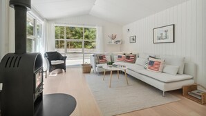 Een moderne woonkamer met een open haard, een bank met patriottische kussens, een rieten fauteuil en een salontafel.