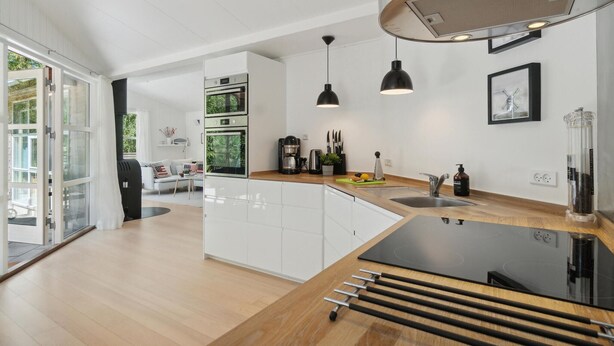 Een moderne keuken met witte kasten, een zwart aanrecht en een ingebouwde kookplaat. Er zijn twee hanglampen, een koffiezetapparaat en een spoelbak.