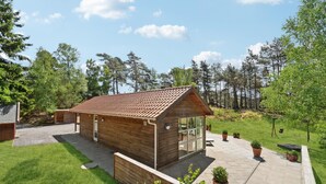 Een klein houten huisje met een pannendak, een glazen deur en een geplaveid terras met potplanten.