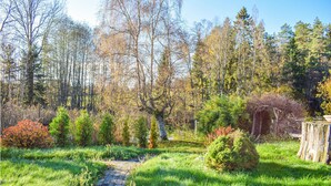 A stone pathway leading through a lush garden with various shrubs and trees. - Lovely home in Huskvarna (Huskvarna)