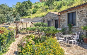 Un edificio in pietra con patio, posti a sedere all'aperto e un giardino ricco di piante e fiori.