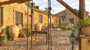A cobblestone courtyard with a wooden swing, stone buildings, and potted plants. - Stunning home in Ficarra (Ficarra)