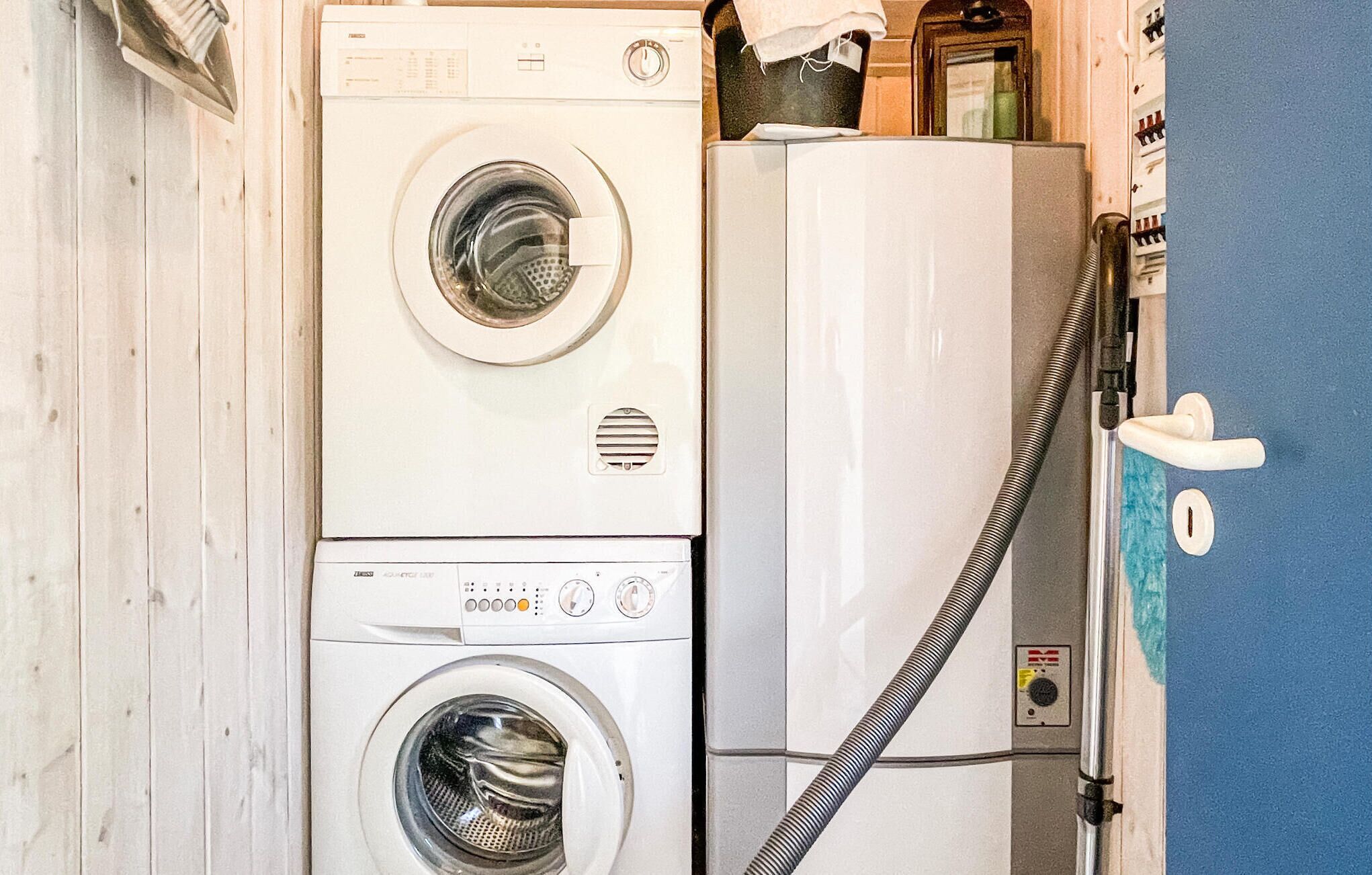 Een wasruimte met een gestapelde wasmachine en droger, een slang en een blauwe muur.