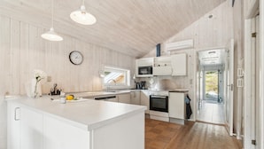 Ett modernt kök med vita skåp, en köksö, en mikrovågsugn, en ugn och en klocka på väggen.