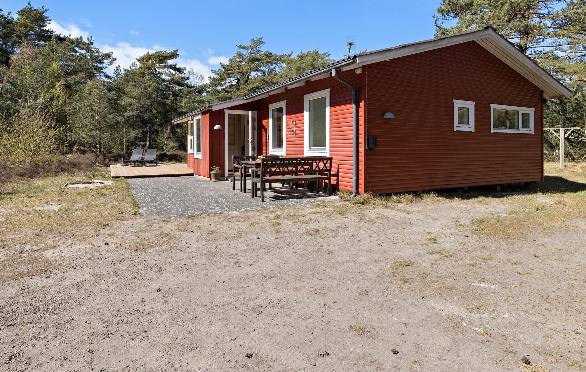 Une cabane rouge avec une véranda, une table et deux chaises.
