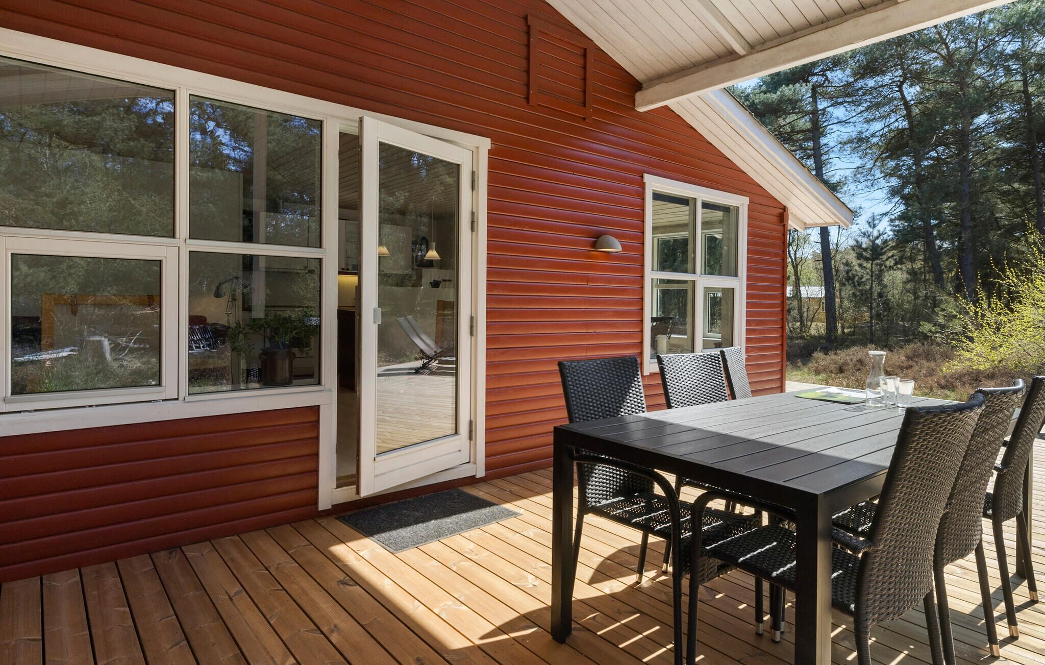 A wooden deck with a table and chairs, a sliding glass door, and a small outdoor light fixture.