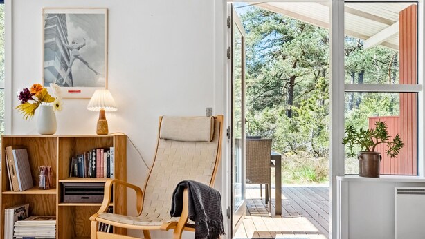 Een gezellige kamer met een houten stoel, een boekenplank, een lamp en een raam met uitzicht op bomen.