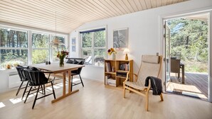 Een modern interieur met een houten plafond, grote ramen, een eettafel met stoelen, een boekenkast en een bankje.