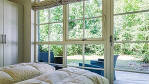 Une chambre avec deux lits, une grande fenêtre et une vue sur la verdure.