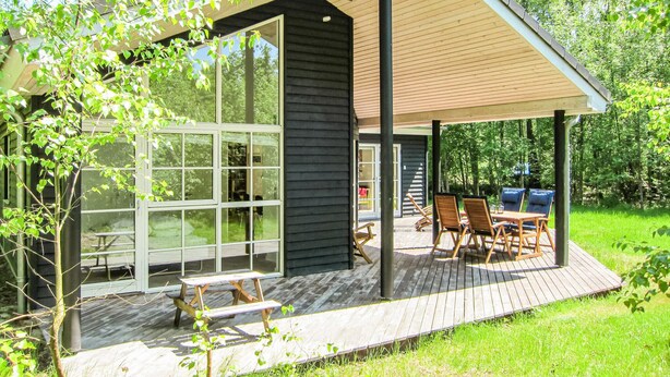 Une maison moderne dotée d’un patio couvert, de grandes fenêtres et d’un espace salon extérieur.