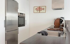 Una cuina compacta amb nevera d'acer inoxidable, forn i un rentamànega amb aixeta moderna.