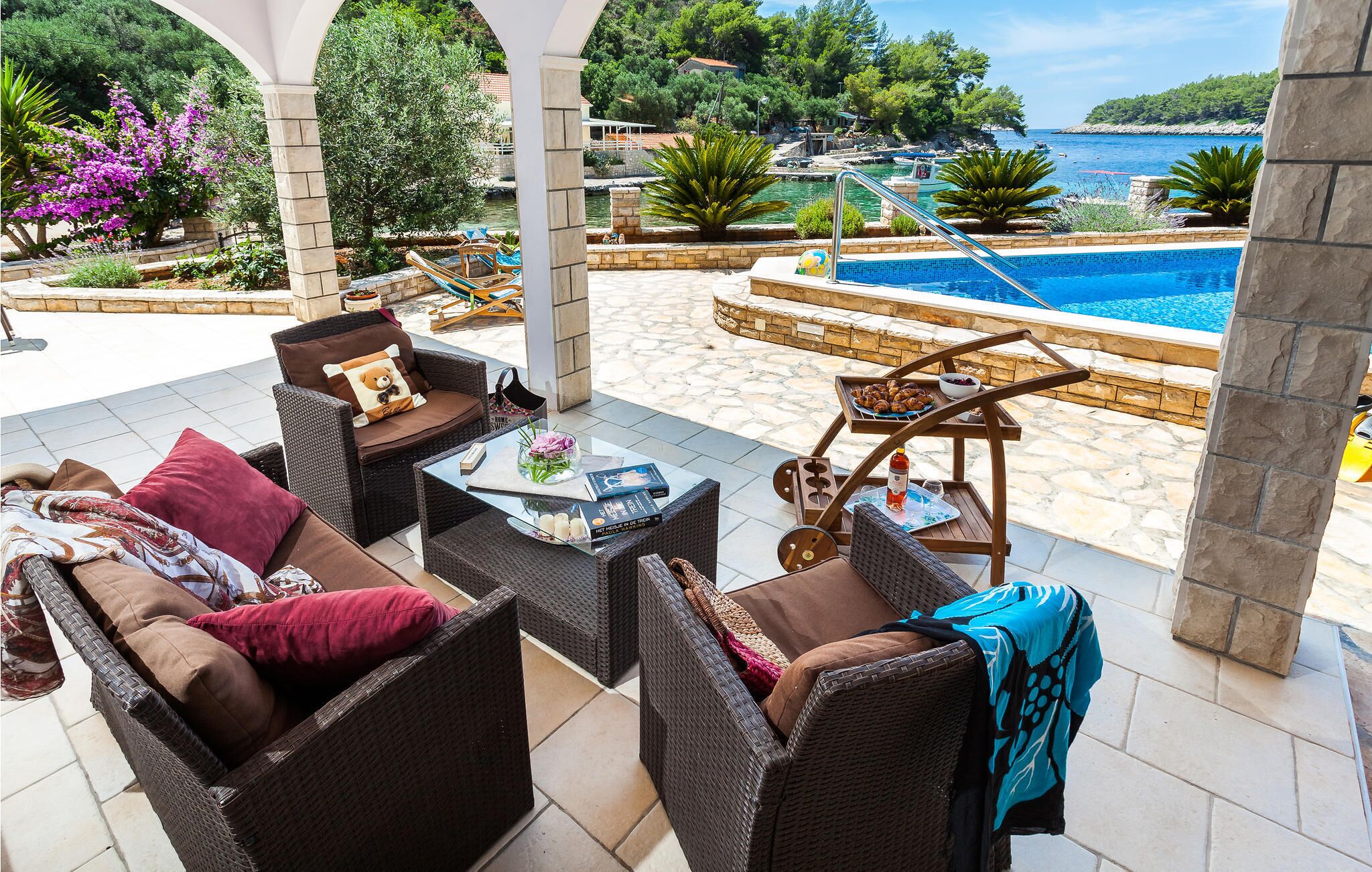 Een overdekt terras met rieten meubels, een zwembad en uitzicht op zee.