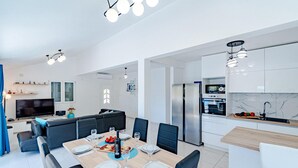 A modern kitchen with a built-in oven and microwave, a dining area with a wooden table set for four, and a living area with a sofa and TV.