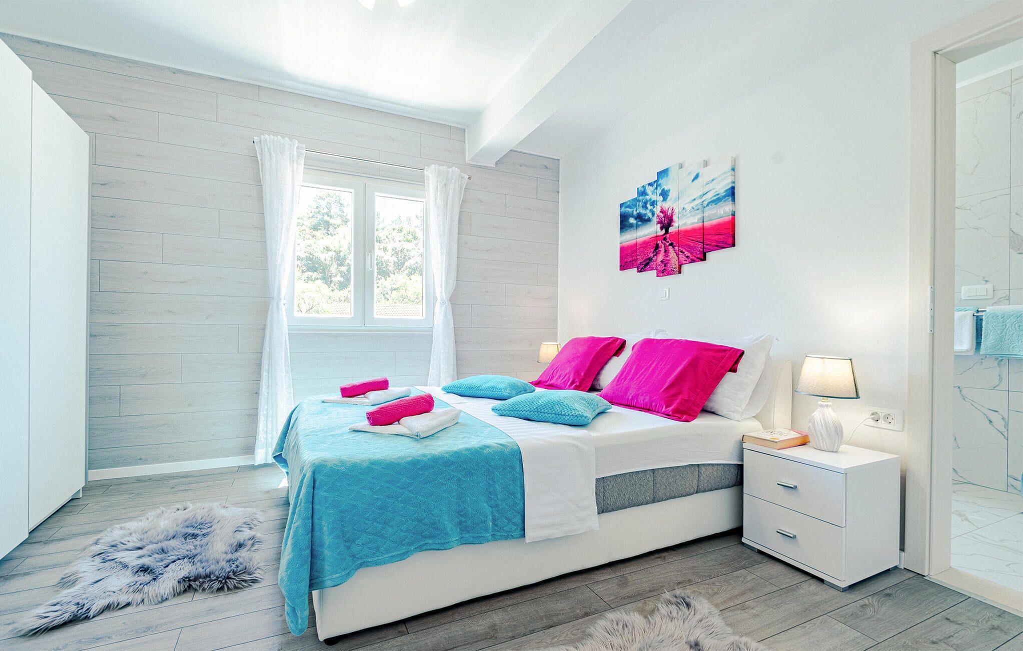Une chambre moderne avec un grand lit, des tables de chevet blanches, un tapis moelleux et une fenêtre ornée de rideaux légers.