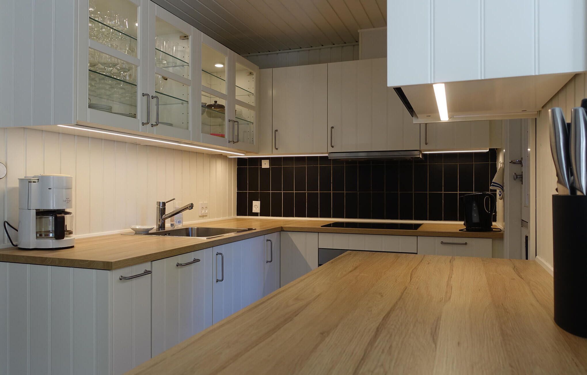 Una cocina moderna con armarios blancos, salpicadero negro y encimera de madera.