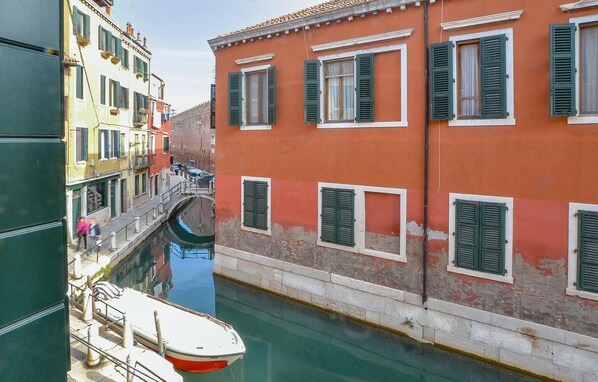 A narrow canal with a boat docked on the left, flanked by buildings with green shutters and a red facade. - Gorgeous apartment in Venezia with WiFi (Venezia)