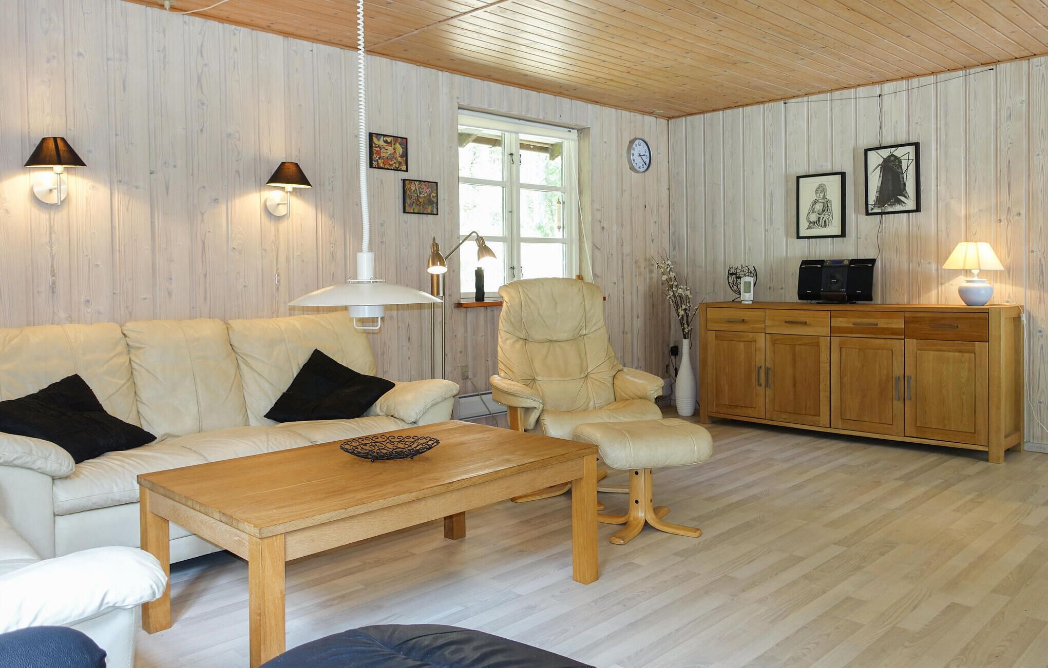 Un salon confortable avec un canapé, un fauteuil, une table basse en bois et un meuble sur lequel est posée une télévision.