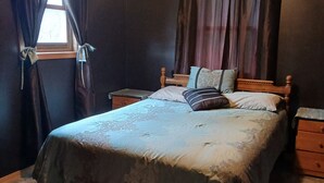 A bedroom with a large bed, two nightstands, a wooden headboard, and a window with curtains. -  Cozy home in Wisconsin's recreational northwoods. (Butternut)