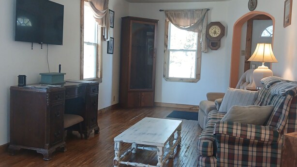 A living room with a wooden floor, a television mounted on the wall, a desk with a chair, a sofa, and a lamp. -  Cozy home in Wisconsin's recreational northwoods. (Butternut)