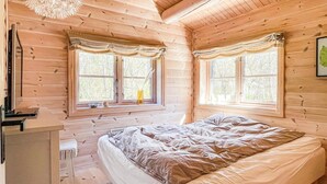 A wooden cabin bedroom with two windows, a bed, a nightstand, and a small table. - Lovely home in Nexø with kitchen (Nexø)
