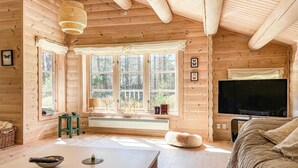 A cozy log cabin interior with a large window, a television, and a fireplace. - Lovely home in Nexø with kitchen (Nexø)