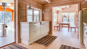 A wooden cabin interior with a kitchen, dining area, and a large window providing a view of the outdoors. - Lovely home in Nexø with kitchen (Nexø)