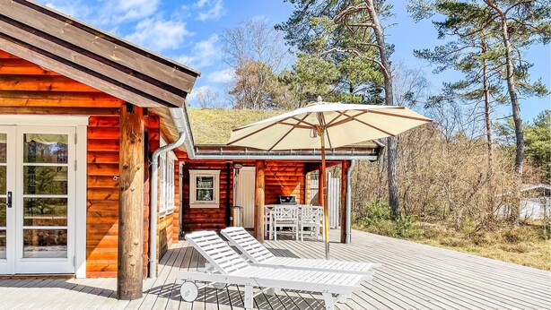 A wooden cabin with a deck, a covered outdoor seating area, and a view of the surrounding forest. - Lovely home in Nexø with kitchen (Nexø)