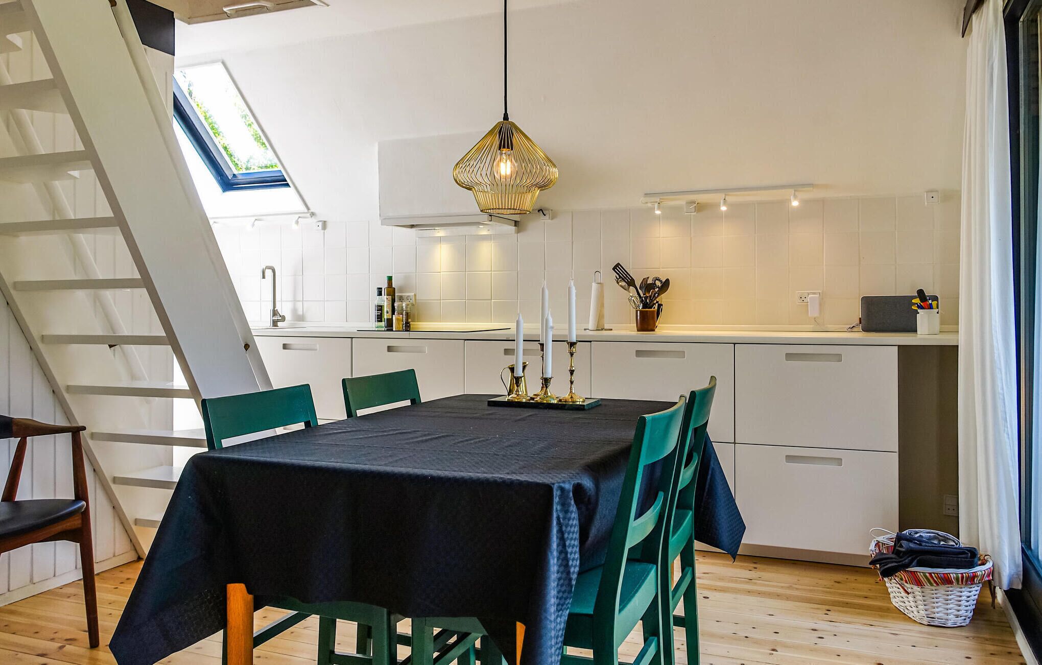 Una cocina moderna con armarios blancos, un comedor con mesa negra y sillas verdes.