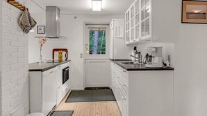 A compact kitchen with white cabinetry, a built-in oven, a coffee maker, and a window with a view of trees.
