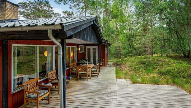 A wooden deck with outdoor seating, a covered area with a door labeled "PRIVATE," and a view of the surrounding forest.