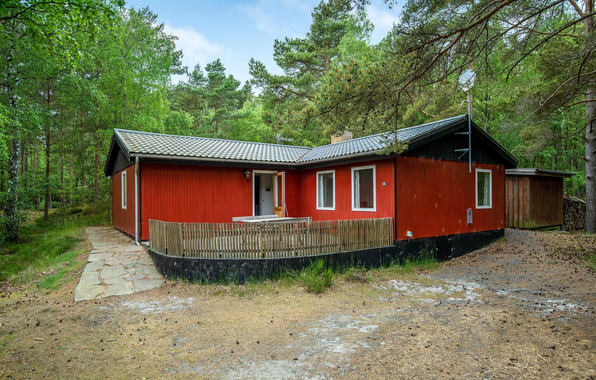 Een rode blokhut met een houten terras, omgeven door bomen.