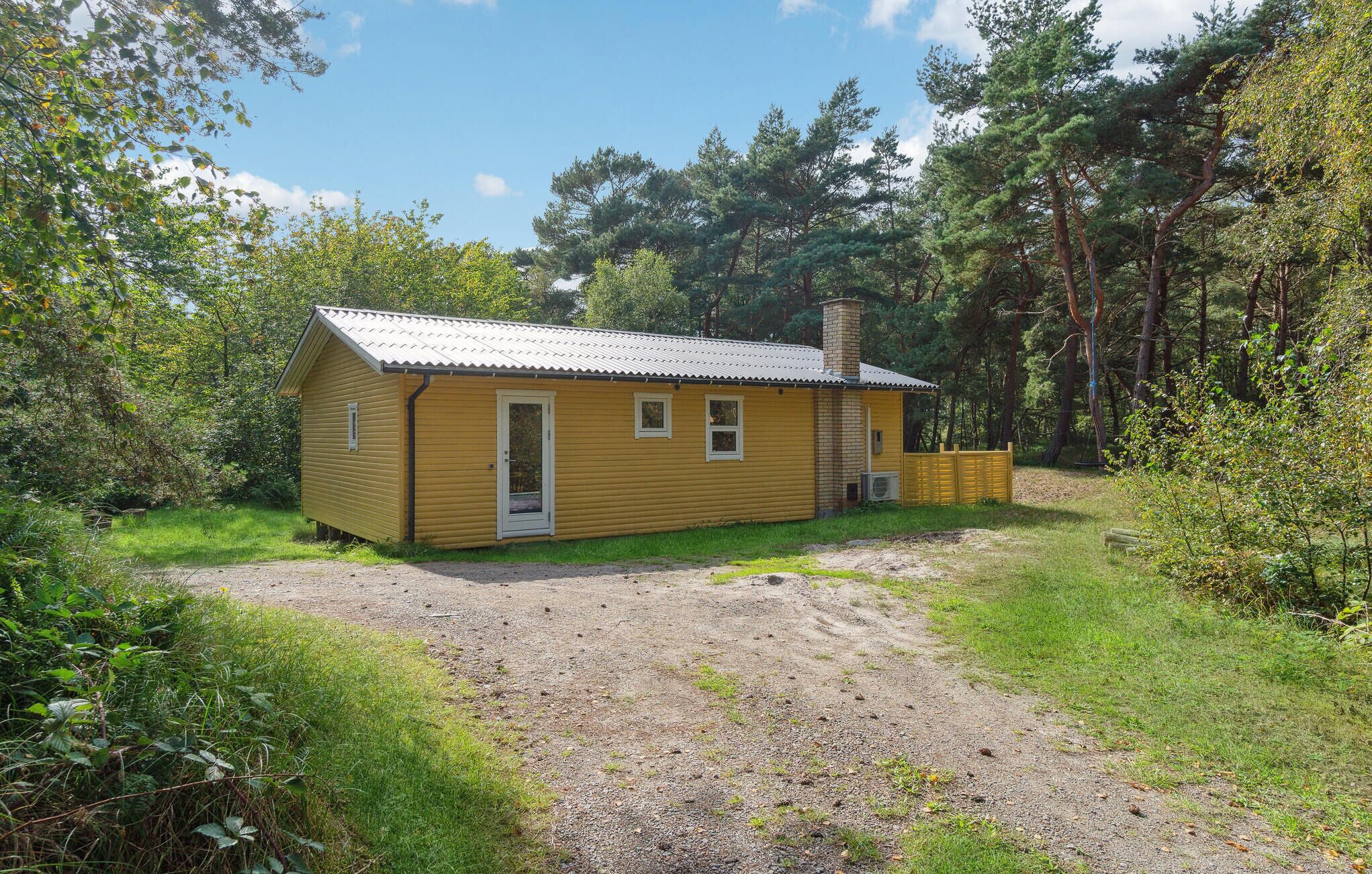 A small yellow cabin with a metal roof, surrounded by dense forest.