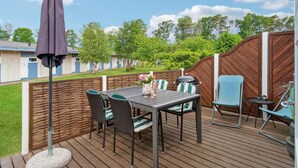 Um terraço com mesa e cadeiras, churrasqueira e vista para uma área residencial com casas e árvores.