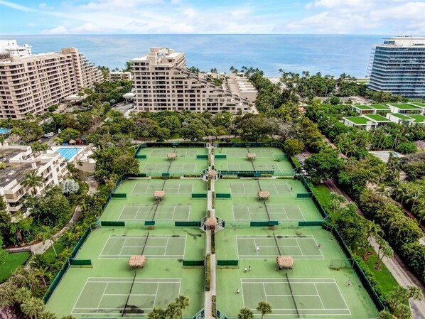 Ein großer Tennisplatzkomplex, umgeben von üppiger Vegetation und Hochhäusern.