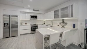 A modern kitchen with white cabinetry, stainless steel appliances, and a marble countertop. - KEY BISCAYNE LUXURY RETREAT - FULLY REMOLEDED 3 BEDROOM 2,000 SF RESIDENCE (Miami)