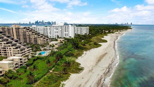A coastal hotel with multiple high-rise buildings, a beach, and a city skyline in the background. - KEY BISCAYNE LUXURY RETREAT - FULLY REMOLEDED 3 BEDROOM 2,000 SF RESIDENCE (Miami)