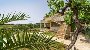 A stone villa with a patio, surrounded by lush greenery and a vineyard.