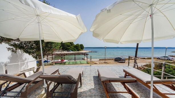 A beachside lounge with wooden loungers and white umbrellas, overlooking the sea.