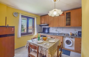 A kitchen with wooden cabinets, a dining table set for four, a washing machine, and a window with curtains. - Amazing apartment in Ricadi with house sea view (Ricadi)