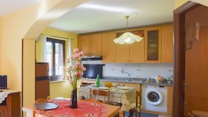 A kitchen with wooden cabinets, a washing machine, a dining table with a red tablecloth, and a vase with flowers.